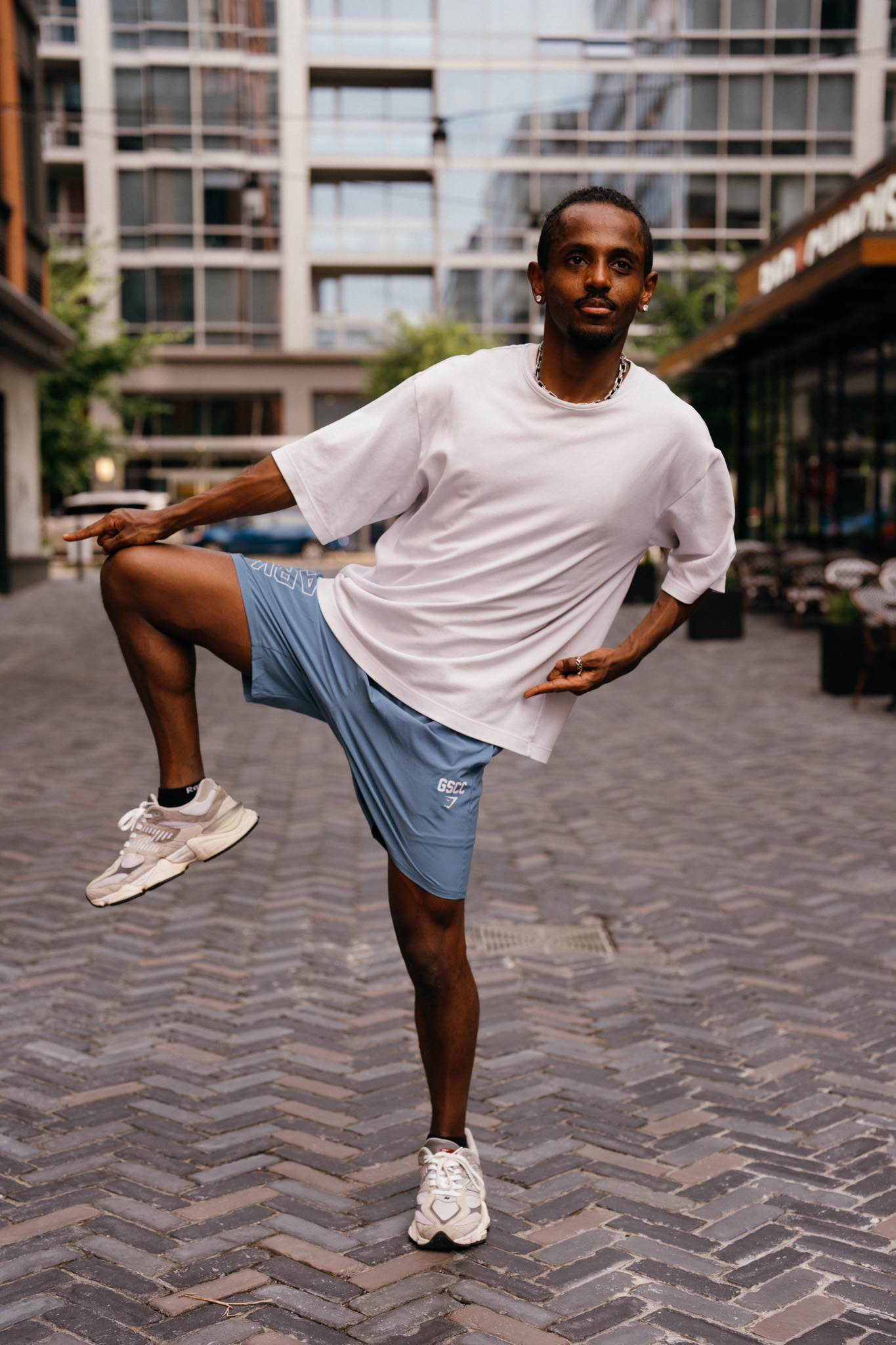 Meni dancing with one leg raised looking directly at camera, Crystal City courtyard, July 2026.