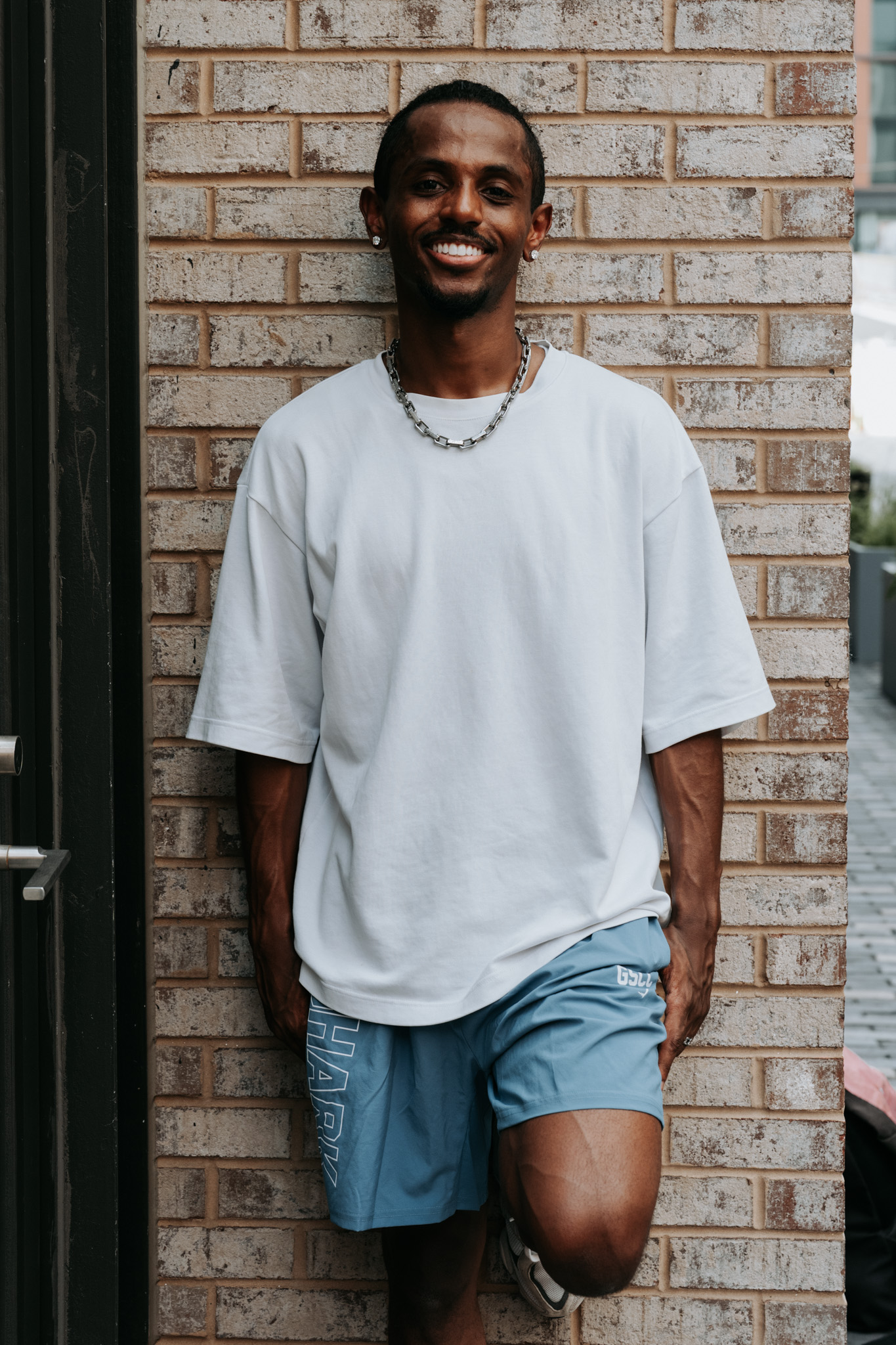 Meni full body leaning against a brick wall smiling, Crystal City, July 2026.