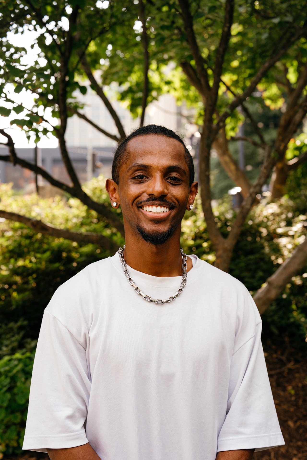 Meni close portrait smiling with green tree bokeh background, Crystal City, July 2026.