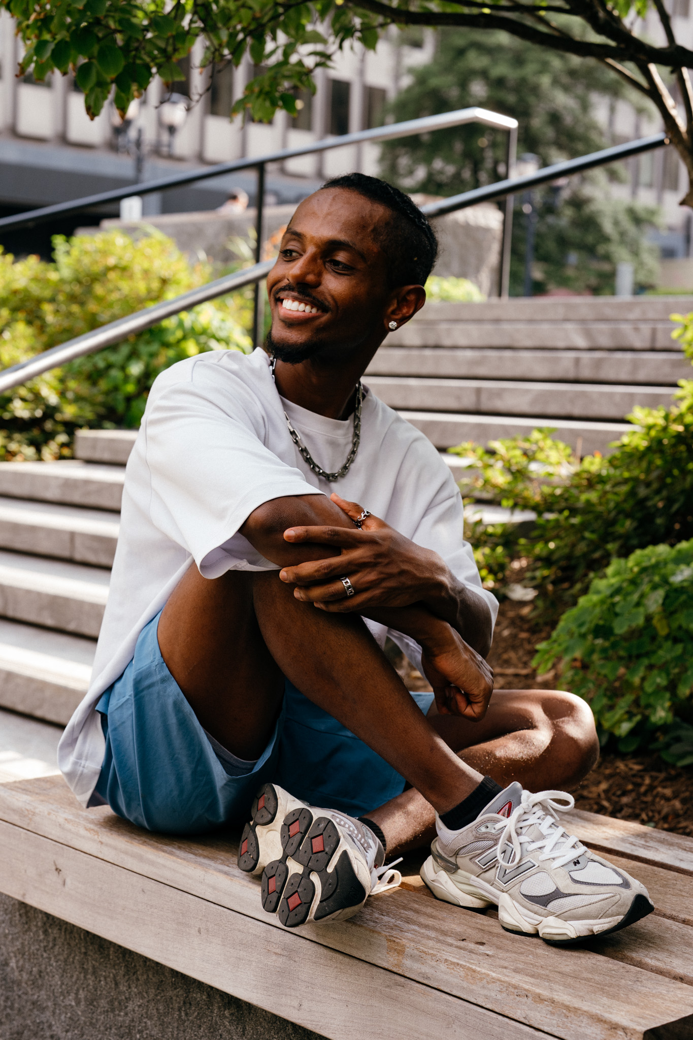 Meni seated on steps with a candid laugh, arms around knees, Crystal City, July 2026.