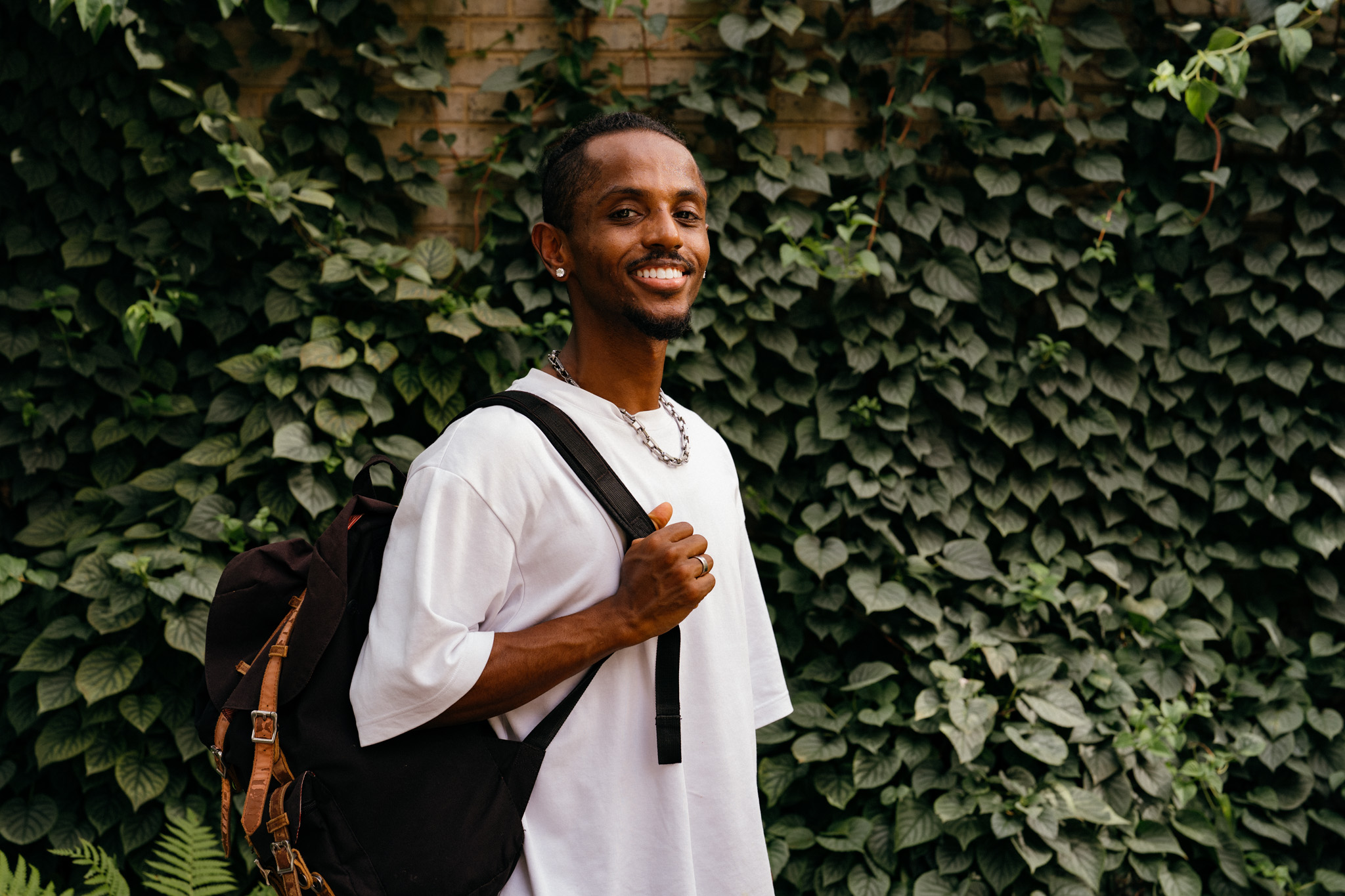 Meni standing with backpack smiling in front of an ivy-covered wall, Crystal City, July 2026.